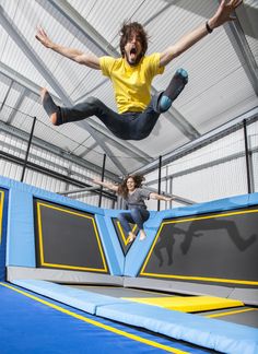 two people are jumping on a trampoline in an indoor area with blue and yellow walls