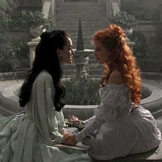 two women dressed in white sitting next to each other on a stone bench and one is holding the hand of another woman's hand