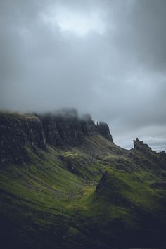 the mountains are covered with green grass and clouds in the distance is a body of water