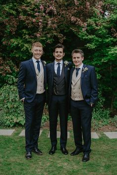 three men standing next to each other in suits and ties on grass with trees in the background