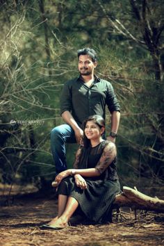 a man and woman sitting next to each other on the ground in front of trees