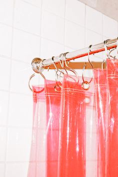 the shower curtain is pink in color and has metal hooks hanging from it's rod