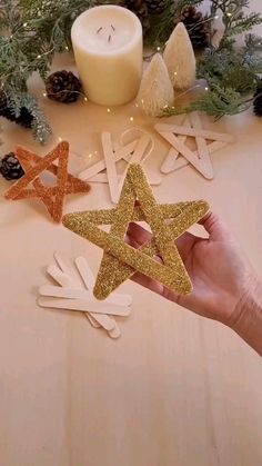 someone is holding up some glittered stars on a table next to candles and pine cones