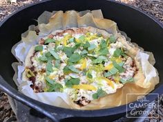 a pizza sitting inside of a black pan on top of a table next to leaves