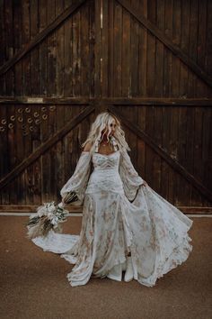 a woman in a white wedding dress holding a bouquet with her arms behind her back