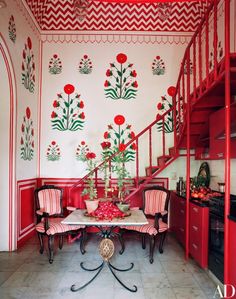 a red and white dining room with flowers painted on the walls, stairs to the second floor