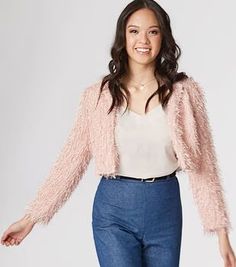 a woman is standing in front of a white background wearing blue jeans and a pink jacket