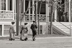 three people are walking down the street in front of a building with balconies