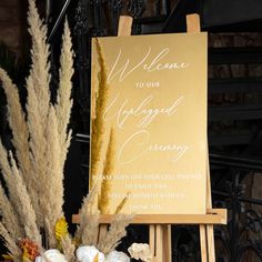 a welcome sign sitting on top of a wooden easel next to flowers and plants