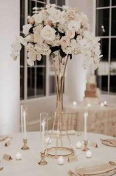 a tall vase filled with white flowers sitting on top of a table next to candles