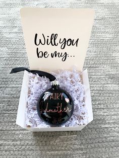 a christmas ornament in a box that says, will you be my?