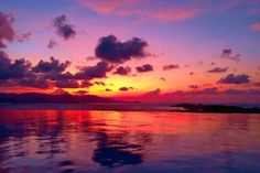 the sun is setting over water with clouds in the sky and mountains in the distance