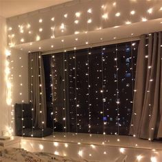 a bedroom with lights hanging from the ceiling and curtains on the window sill over the bed