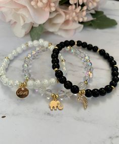 "Beautiful stretch bead bracelets with gold charms and 6mm white marble, crystal or black onyx beads, as well as gold spacers. This listing is for one bracelet with one charm. If you're looking for another color, send me a message! The bracelets shown are approximately 7\" in length. The charm options shown are gold 18k gold plated moon with cubic zirconia charms, light gold elephant and light gold alloy flat round with \"love\"." Charm Beads Bracelet, Beads Bracelet With Charms, Beads Charm Bracelet, White And Black Bracelet, Crystal Beaded Bracelets Diy, Black Crystal Bracelet, Cute Charm Bracelet, Beads Bracelet Making, Handmade Bracelets With Beads