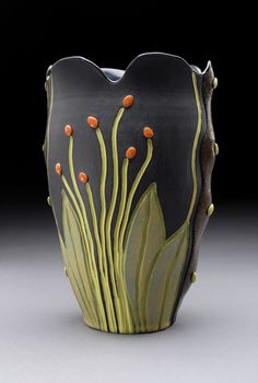 a black vase with orange flowers and green leaves on it's sides, against a dark background