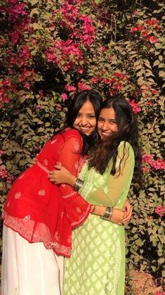 two young women hugging each other in front of some pink and green flowers on a wall