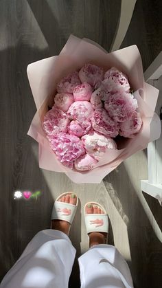 a bouquet of pink flowers sitting on top of a person's feet in white sandals