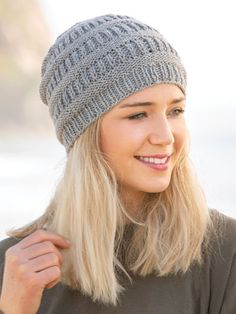 a woman with blonde hair wearing a gray knitted hat and smiling at the camera