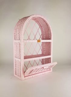 a pink wicker book shelf with an arched window on the top and bottom section