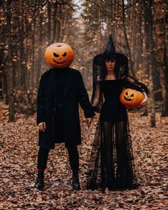 two people dressed up in halloween costumes holding hands and walking through the woods with pumpkins on their heads