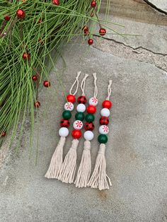 four tasseled beads with red, white and green decorations hanging from the side of a pine tree