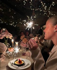 a woman sitting at a dinner table with sparklers in the air