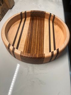 a wooden bowl sitting on top of a counter next to a white counter with a black and brown stripe design