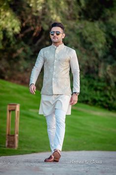 a man in a white suit and sunglasses walking down a path with trees in the background