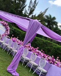 an outdoor wedding setup with purple draping and flowers on the table, along with white chairs