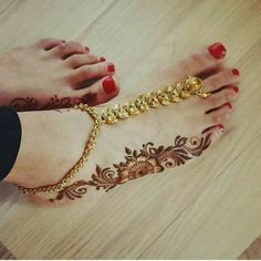 a woman's feet with hennap and gold chains on them, sitting on a wooden floor