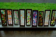 five different colored paintings are displayed on a window sill with grass in the background