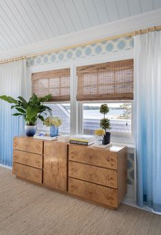 two plants are sitting on top of a dresser in front of a window with blue curtains