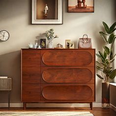 a wooden dresser sitting next to a wall with pictures on it and a clock above it