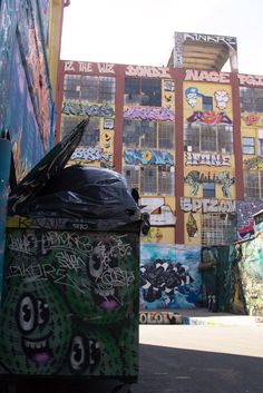 a trash can sitting in front of a building covered in graffiti