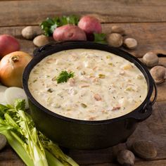 a black pot filled with white sauce next to vegetables and potatoes on a wooden table