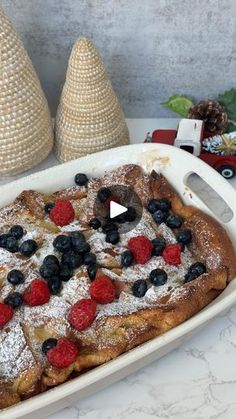 a pan filled with french toast covered in berries and powdered sugar on top of a table