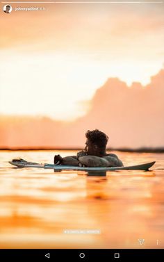 a man laying on top of a surfboard in the middle of water at sunset