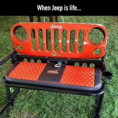 an orange jeep seat sitting on top of a green grass covered field next to a tree