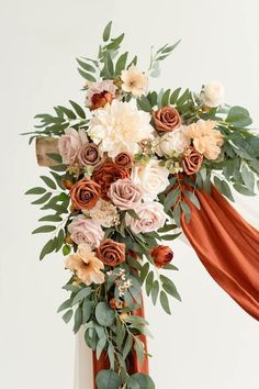 an arrangement of flowers and greenery is displayed on a stand with orange drapes