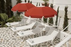 some white lawn chairs and red umbrellas on a patio