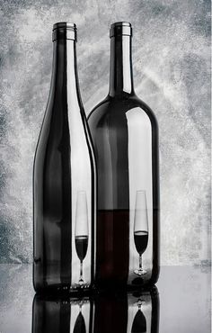 two empty wine bottles and one filled with red wine are sitting on a reflective surface