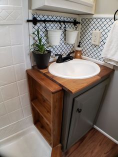 a white sink sitting under a mirror next to a wooden cabinet and potted plant