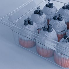 cupcakes with blueberries and cherries are in a plastic container on a white surface