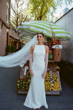 a woman standing in front of a fruit stand with an umbrella over her head,