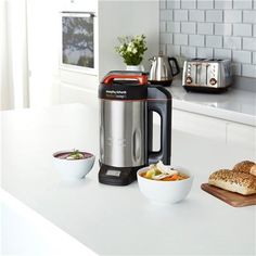 a blender sitting on top of a white counter next to bowls of food in front of it