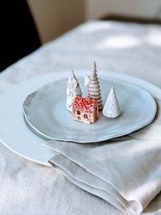 a white plate topped with a small house next to two christmas trees on top of it