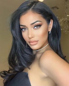 a woman with long black hair and blue eyes posing for a photo in front of a chandelier