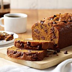 a loaf of chocolate chip pumpkin bread on a cutting board next to a cup of coffee