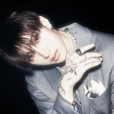 a man in a suit with tattoos on his arm and hand resting against his face