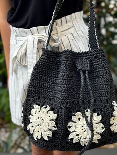 a crocheted black purse with white flowers on the front and side, held by a woman's hand